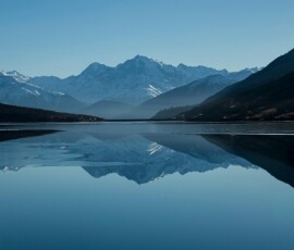 Mountain lake reflecting snow-capped peaks under blue sky