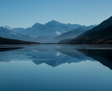 Mountain lake reflecting snow-capped peaks under blue sky