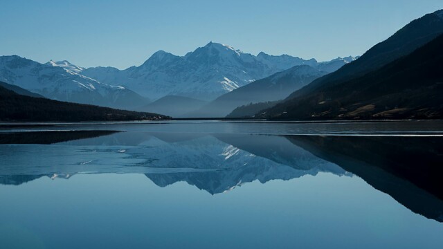 Mountain lake reflecting snow-capped peaks under blue sky